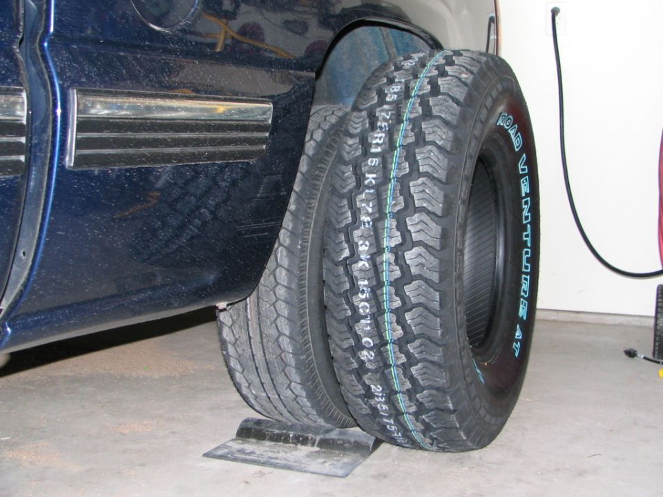 Two Road Venture all-terrain tires leaning against a dark pickup in a garage