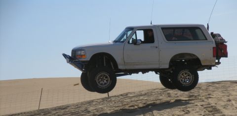 1984 Ford Bronco - A modified Ford Bronco is captured mid-air while traversing a sandy terrain, its off-road capabilities.