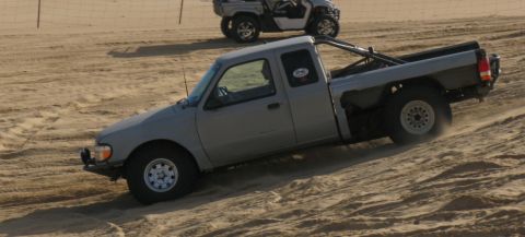 1984 Ford Bronco - A gray pickup truck navigates a sandy incline, with another vehicle visible in the background.