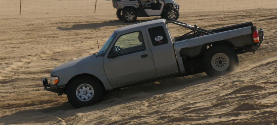 Gray pickup truck with a roll bar driving up a sand dune