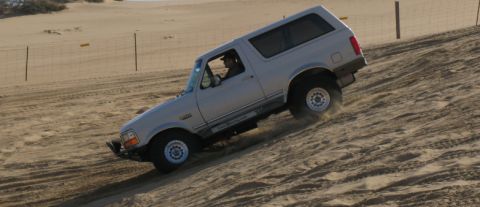 1984 Ford Bronco - Ford Bronco navigates a steep sand dune, showing off its off-road capability.