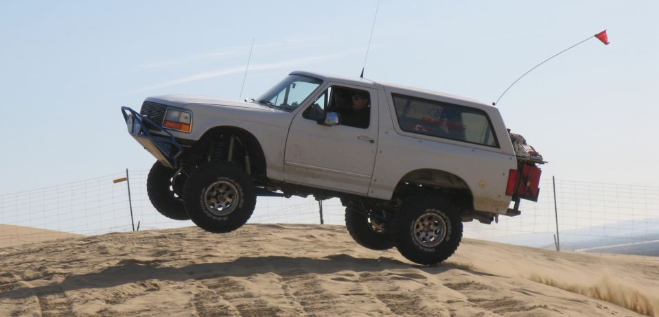 White Ford Bronco with aftermarket bumper and lift kit airborne over sand dune