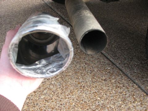 1991 Ford Bronco - A new exhaust pipe is held up next to the old one on a vehicle.