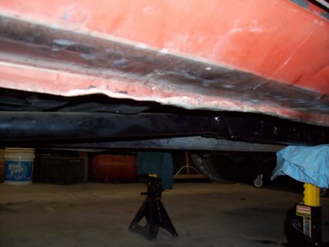 1979 Chevrolet Camaro - Underside view of an orange vehicle supported by jack stands in a garage.