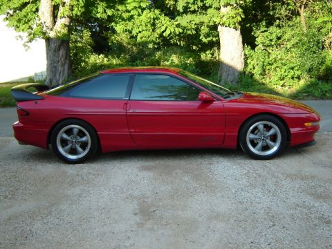 1993 Ford Probe - A red 1993 Ford Probe coupe is shown from the side, parked outdoors with trees in the background.