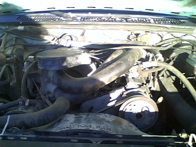 Engine bay with visible hoses and belts. "CAUTION FAN" text visible