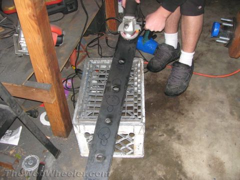 1987 Suzuki Samurai - A person grinds a metal rock slider, which is resting on a plastic crate, with an angle grinder in a workshop.