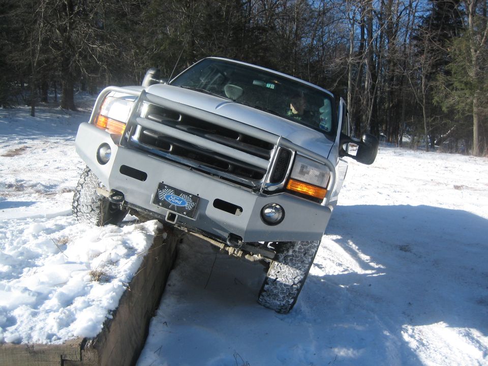 Ford pickup truck with custom bumper driving over snow and wood obstacles