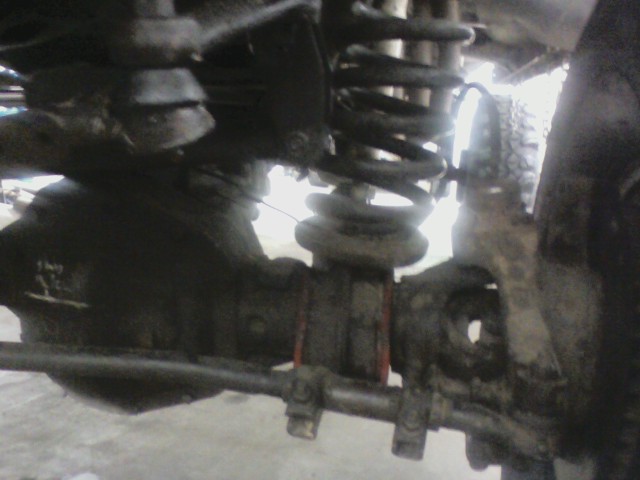 Close-up of a vehicle's front axle, coil spring, and suspension parts