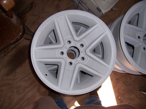 1979 Chevrolet Camaro - Two unfinished five-spoke wheels are stacked on a wooden floor, with a chair visible to the left.