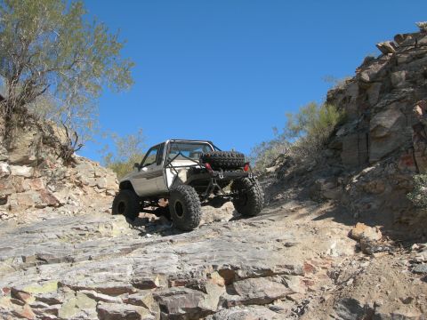 1986 Toyota Hilux - Modified pickup truck navigates a challenging rocky terrain under a clear blue sky.