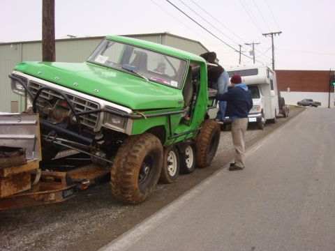 1978 Ford Bronco - A heavily modified green truck with six wheels is being loaded onto a trailer, with several people around it.