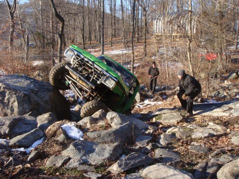 1978 Ford Bronco - A green off-road vehicle navigates a rocky terrain, with two individuals observing the challenging maneuver.