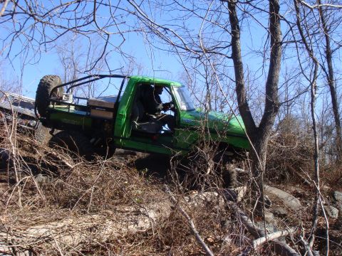 1978 Ford Bronco - Off-road pickup truck navigates challenging terrain on a wooded slope.