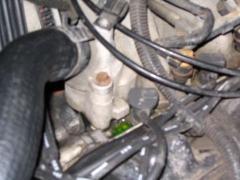 1995 Mercury Grand Marquis - Tight engine-bay shot of a cast aluminum thermostat housing / coolant crossover with a corroded nipple, surrounded by a large black upper r…