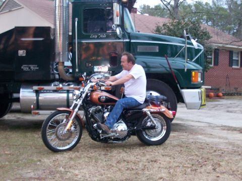 1996 Ford Bronco - A man rides a motorcycle in front of a large green semi-truck.