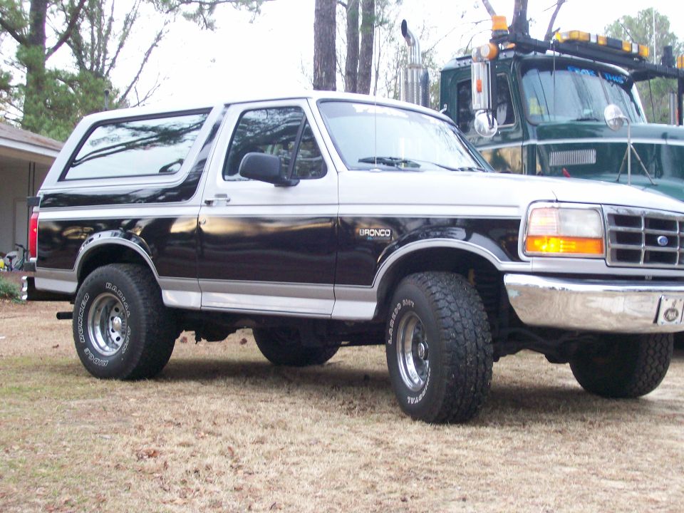 Two-tone Ford Bronco parked next to a green tow truck