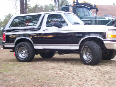1996 Ford Bronco - A two-tone black and silver Ford Bronco is parked on grass, with a green tow truck visible in the background.