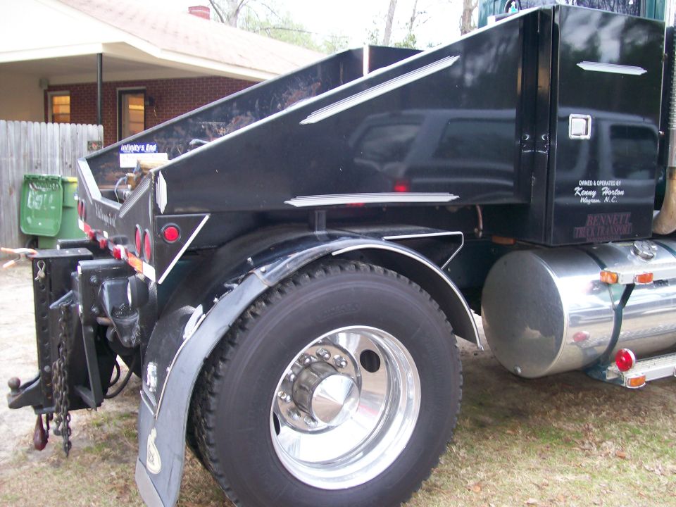 Black dump truck bed with chrome accents, rear wheel, and fuel tank