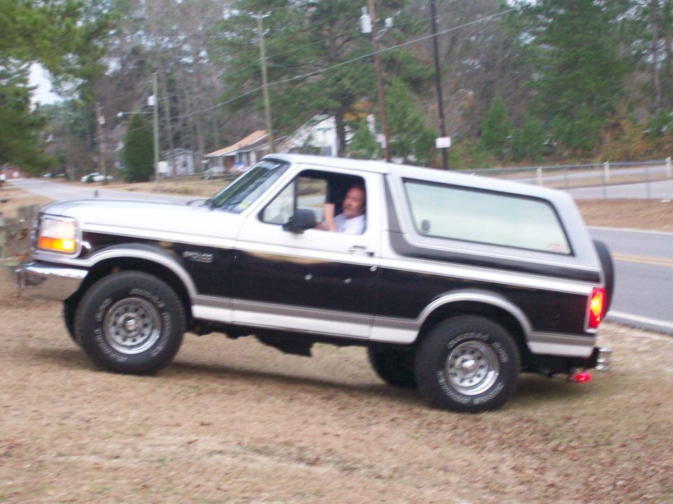 1996 Ford Bronco with a man driving, two-tone black and silver paint, parked on a dirt incline