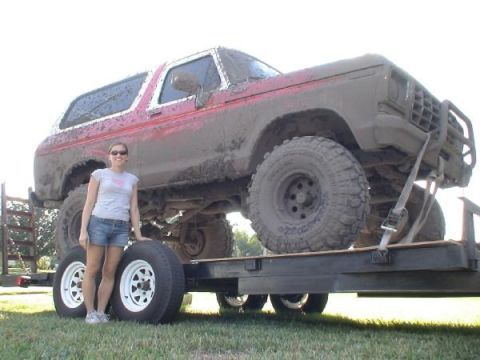 1978 Ford Bronco - A woman stands beside a heavily mud-covered 1978 Ford Bronco loaded onto a trailer.