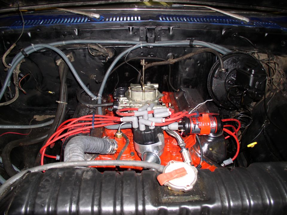Orange V8 engine bay with chrome carburetor, red plug wires and distributor