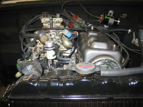 1987 Suzuki Samurai - Close-up of an engine bay, a carburetor and radiator. The radiator cap has warning text.