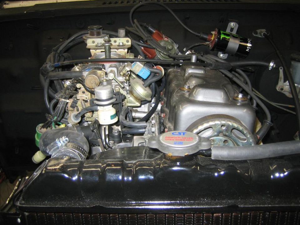 Engine bay showing carburetor, distributor, and radiator cap. Text on cap reads 'CST DANGER HOT'