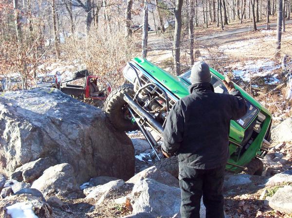 Green off-road vehicle tilted on rocks, with a red vehicle behind it