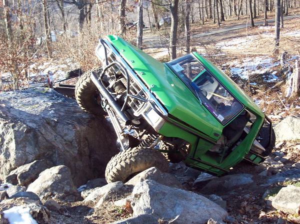 Green off-road vehicle tilted on rocks with a winch on the front
