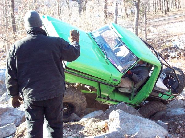 1978 Ford Bronco tilted on its side, stuck between large rocks on a wooded trail