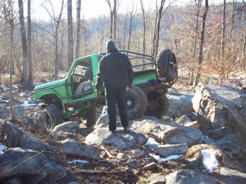 1978 Ford Bronco - A modified green off-road vehicle navigates a rocky terrain with a person standing nearby.