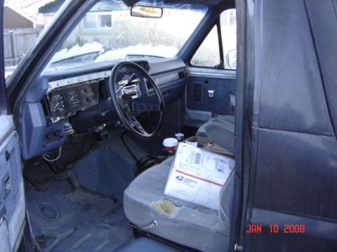 1985 Ford Bronco - The interior of a 1985 Ford Bronco, a blue dashboard and seats, with a package on the passenger seat.