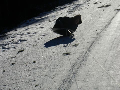 1978 Ford Bronco - Person on a sled being pulled up a snowy hill, with tire tracks visible on the ground.