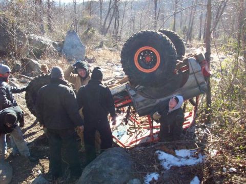 1978 Ford Bronco - Several people gather around an overturned off-road vehicle in a wooded, rocky terrain.