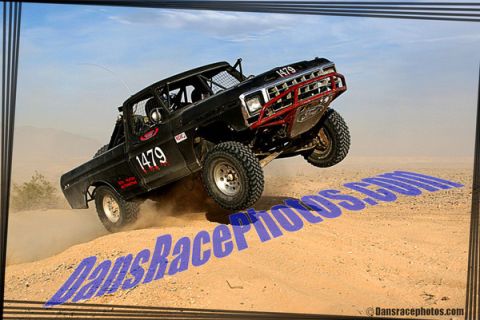 1986 Ford Bronco - This modified truck is airborne during a desert race, kicking up dust as it goes.