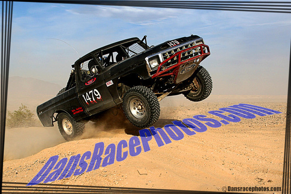 Black off-road truck with red bull bar jumping over sand dune. Number 1479 on door