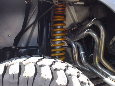 1986 Ford Bronco - Close-up view of a vehicle's suspension and exhaust components, including a large off-road tire.