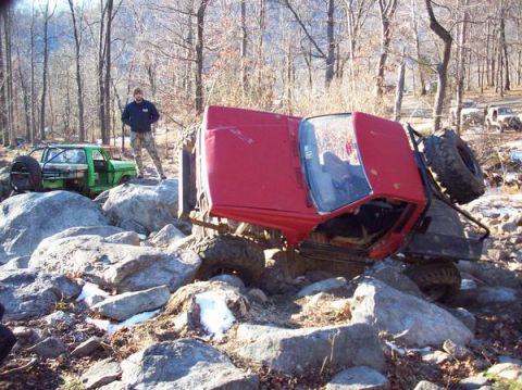 1978 Ford Bronco - A red 1978 Ford Bronco is overturned on a rocky trail, with a green off-road vehicle visible in the background.