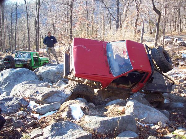 Red 1978 Ford Bronco overturned on rocks, green off-road vehicle nearby