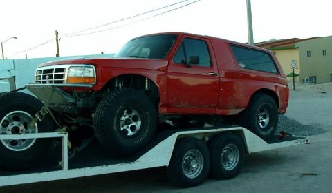 1986 Ford Bronco - This red Ford Bronco is being transported on a trailer, showing off its lifted suspension and large off-road tires.