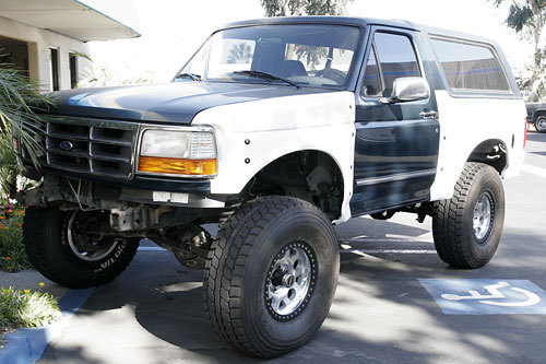 Ford Bronco with a two-tone paint job, lifted suspension, and off-road tires parked in a lot