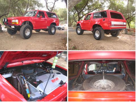 1986 Ford Bronco - Modified red Ford Bronco, lifted with large tires, showing engine bay and interior with roll cage.