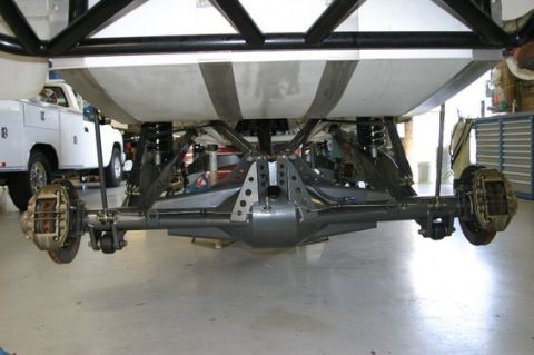 1986 Ford Bronco - The rear axle and suspension components of a vehicle are visible, with a white service truck in the background.