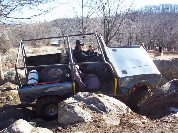 Off-road vehicle with roll cage navigating rocks; spare tire visible in rear