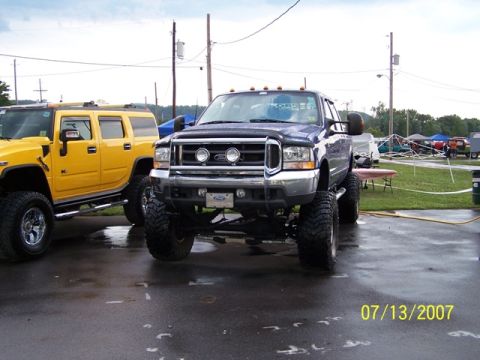 2003 Ford F-250 - A dark blue 2003 Ford F-250 pickup truck with a lifted suspension and oversized tires is parked next to a yellow Hummer.