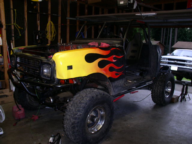 Black 4x4 project truck with yellow flame-painted hood, doors and top removed, in a garage