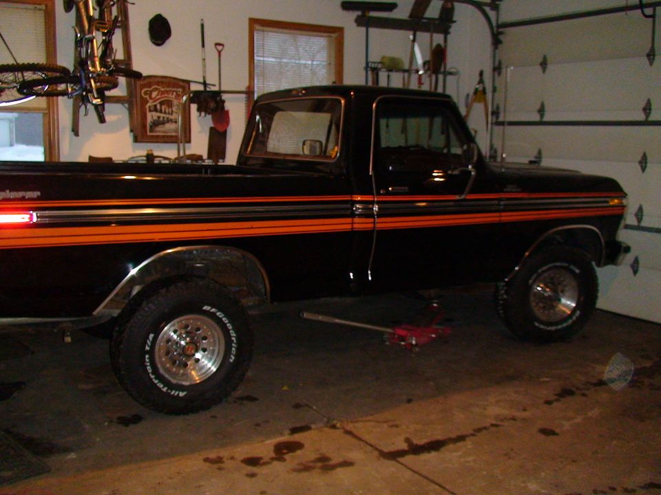 Black 1979 Ford F-150 pickup truck with orange side stripes, in a garage with a jack under the front wheel
