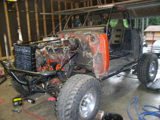 Off-road buggy under construction, orange fender, exposed engine, roll cage, large tires