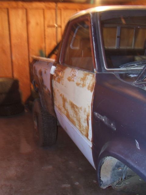 1990 Ford Bronco - Pickup truck body in disrepair, with visible rust and primer patches on the fender and door.